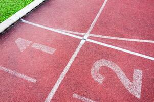 Zahlen beginnend Punkt auf rot Laufen verfolgen, laufen Spur und Grün Gras, direkt Leichtathletik Laufen Spur beim Sport Stadion foto