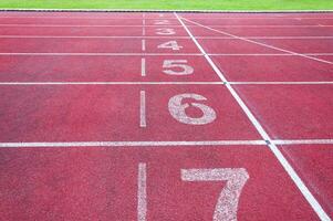 Zahlen beginnend Punkt auf rot Laufen verfolgen, laufen Spur und Grün Gras, direkt Leichtathletik Laufen Spur beim Sport Stadion foto