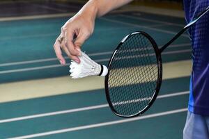 Badminton Spieler hält Schläger und Weiß Sahne Federball im Vorderseite von das Netz Vor Portion es zu Ein weiterer Seite von das Gericht foto