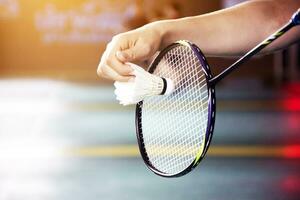 Badminton Spieler hält Schläger und Weiß Sahne Federball im Vorderseite von das Netz Vor Portion es zu Ein weiterer Seite von das Gericht foto