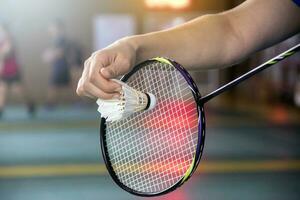 Badminton Spieler hält Schläger und Weiß Sahne Federball im Vorderseite von das Netz Vor Portion es zu Ein weiterer Seite von das Gericht foto