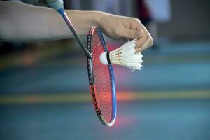 Badminton Spieler hält Schläger und Weiß Sahne Federball im Vorderseite von das Netz Vor Portion es zu Ein weiterer Seite von das Gericht foto