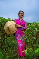 ein indonesisch Frau im ein Rosa Kleid halten ein Bambus Hut im ihr Hände foto