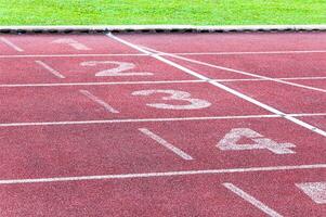 Zahlen beginnend Punkt auf rot Laufen verfolgen, laufen Spur und Grün Gras, direkt Leichtathletik Laufen Spur beim Sport Stadion foto