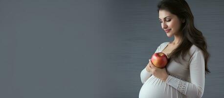 schwanger Frau mit Apfel zum Bauch auf grau Studio Hintergrund Ernährung und Schwangerschaft Konzept Banner mit Kopieren Raum foto