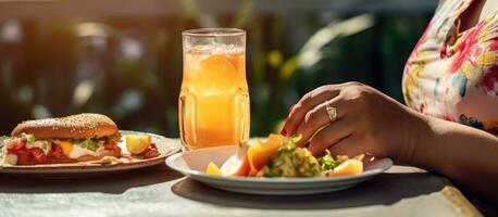 Plus Größe Frau haben Mittagessen draußen nehmen ein Sandwich Scheibe mit ein Gabel Orange Saft auf das Tabelle foto