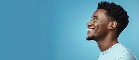 Seite Aussicht von jung afrikanisch amerikanisch Mann lächelnd und suchen beiseite isoliert auf Blau Hintergrund mit Kopieren Raum foto