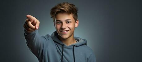 lächelnd Teenager Junge zeigen nach oben im ein Porträt auf ein grau Hintergrund foto