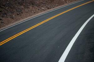 das Asphalt Straße hat Gelb und Weiß der Verkehr Linien Kreuzung das Berge. foto