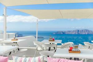 Cafe auf das Terrasse mit Blick auf das Meer. Santorini Insel, Griechenland. hervorragend Sommer- Stimmung, draussen Restaurant. romantisch Schwingungen, Sommer- Farben unter Weiß Zelt und Blau Himmel foto