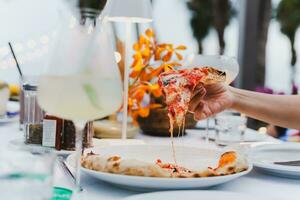 Frau Hand halten Pizza im ein Teller auf Abendessen Tisch. foto