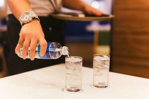 Bedienung Hand Gießen Wasser von Flasche in ein Glas im Restaurant. foto