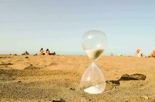 ein Sanduhr auf das Strand mit Menschen im das Hintergrund foto