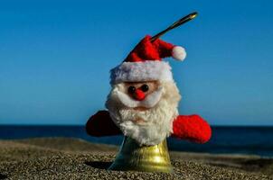 ein Santa claus Spielzeug auf das Strand mit das Ozean im das Hintergrund foto