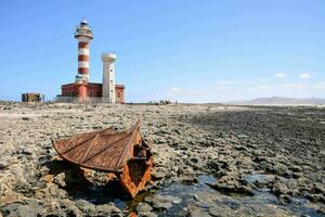 ein alt Boot ist Sitzung auf das Strand in der Nähe von ein Leuchtturm foto