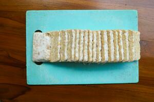 geschnitten frisch roh Tempeh, auf ein Plastik Schneiden Tafel auf ein hölzern Hintergrund. Essen Vorbereitung Konzept foto