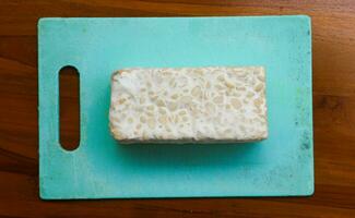 frisch roh Tempeh, auf ein Plastik Schneiden Tafel auf ein hölzern Hintergrund. Essen Vorbereitung Konzept foto