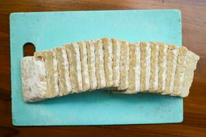 geschnitten frisch roh Tempeh, auf ein Plastik Schneiden Tafel auf ein hölzern Hintergrund. Essen Vorbereitung Konzept foto