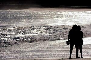 zwei Menschen Stehen auf das Strand mit das Ozean im das Hintergrund foto