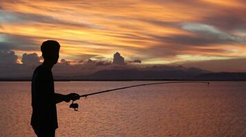 Silhouette von ein Fischer mit ein Angeln Stange im das See beim Sonnenuntergang foto
