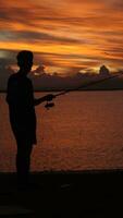 Silhouette von ein Fischer mit ein Angeln Stange im das See beim Sonnenuntergang foto