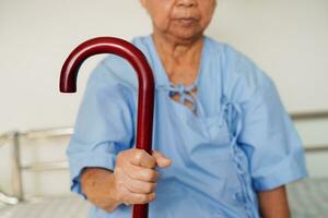 asiatisch Alten Behinderung Frau geduldig halten Gehen Stock im faltig Hand beim Krankenhaus. foto