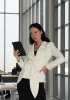 Offenes Porträt einer jungen kaukasischen selbstbewussten Geschäftsfrau, die Tablet verwendet, um im Büro zu arbeiten