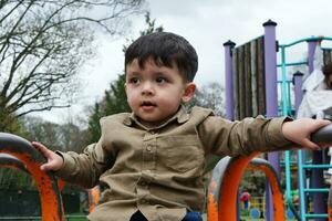 süß asiatisch pakistanisch Baby ist genießen das schön sonnig Tag beim Krieg Kinder und Öffentlichkeit Park von Luton Stadt, Dorf von England Vereinigtes Königreich. niedrig Winkel Bild war gefangen auf April 03., 2023 foto