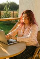 Frau Arbeiten mit Laptop draussen im Sommer- Terrasse. Mädchen Aufpassen Video auf Computer im das Abend. Arbeiten von heim, Geschäft und Lebensstil Konzept. foto