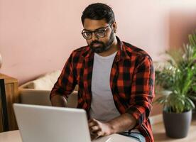 Technologie Fernbedienung Job und Lebensstil Konzept - - glücklich indisch Mann im Brille mit Laptop Computer Arbeiten beim Zuhause Büro foto