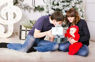 Weihnachten Familie mit Baby Öffnung Geschenke. glücklich lächelnd Eltern und Kind beim Zuhause feiern Neu Jahr foto