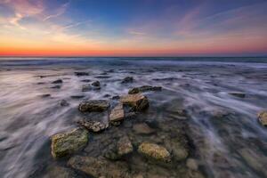 schön felsig Strand mit Steine im verschwommen Wasser, das bunt Himmel beim Sonnenaufgang. schwarz Meer, Bulgarien. Landschaft mit das Meer Wellen und Felsen. foto