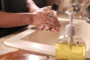 junger Mann, der Hände mit warmem Wasser der Seife wäscht foto