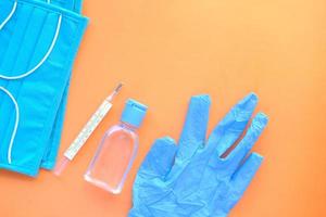 chirurgische Masken, medizinische Handschuhe und Händedesinfektionsmittel auf orangem Hintergrund