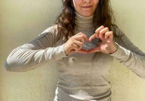 ein Frau zeigt an ein Herz mit ihr Hände. foto
