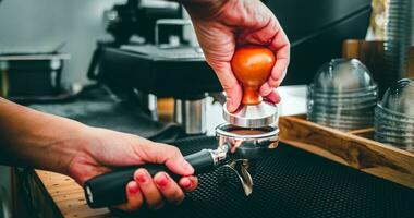 Nahansicht von Hand Barista Cafe Herstellung Kaffee mit Handbuch drückt Boden Kaffee mit ein manipulieren beim das Kaffee Geschäft foto