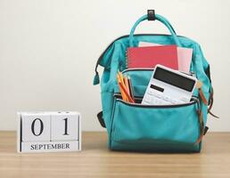 Vorderseite Aussicht von Grün Rucksack mit Schule liefert und hölzern Kalender September 01 auf hölzern Tabelle und Weiß Hintergrund mit Kopieren Raum. foto