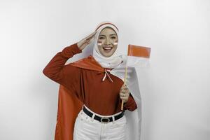 indonesisch Muslim Frau tragen Hijab geben Gruß mit stolz Geste während halten Indonesiens Flagge. Indonesiens Unabhängigkeit Tag Konzept foto