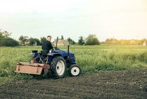 ein Farmer ist Fahren ein Traktor über das Feld. Mühle Mahlen Maschine zum Boden. Land Anbau. Rekrutierung und Einstellung saisonal Arbeiter zum arbeiten. Landwirtschaft, Landwirtschaft. Land Verbesserung, Milderung. foto