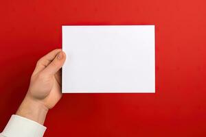 ein Mensch Hand halten ein leer Blatt von Weiß Papier oder Karte isoliert auf rot Hintergrund. ai generiert foto