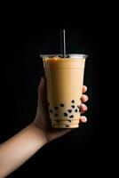 ein Hand halten wegbringen Plastik Tasse von köstlich vereist Blase Milch Tee und schwarz Perlen isoliert auf schwarz Hintergrund. ai generiert foto