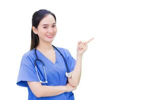 Fachmann jung asiatisch Frau Arzt tragen Blau Uniform und Stethoskop Stehen während zeigen zu das oben mit glücklich und Lächeln beim Untersuchung Zimmer im Krankenhaus während isoliert auf Weiß Hintergrund. foto