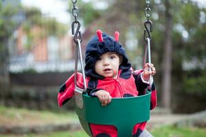 wenig Baby Mädchen tragen ein Marienkäfer Kostüm Sitzung auf ein Kleinkind schwingen. Halloween Konzept. foto