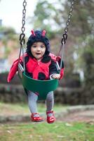 wenig Baby Mädchen tragen ein Marienkäfer Kostüm Sitzung auf ein Kleinkind schwingen. Halloween Konzept. foto