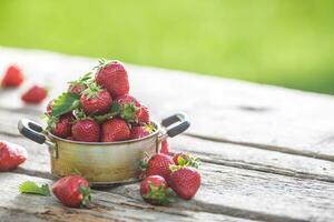 frisch reif Erdbeeren im Jahrgang Küche Topf auf alt Garten Tabelle foto