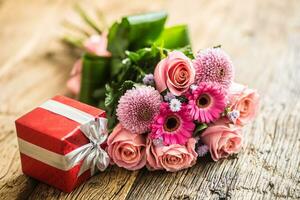 schön Strauß von Blumen mit rot Geschenk auf hölzern Tisch. foto