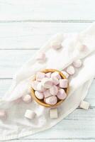 oben Porträt Aussicht von ein hölzern Schüssel voll von Rosa und Weiß Marshmallows mit etwas verstreut um auf ein Weiß Tabelle Stoff foto