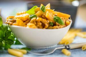 Pasta Penne mit Hähnchen Stücke Pilze Basilikum und Parmesan Käse Italienisch Essen im Weiß Schüssel auf Küche Tabelle foto