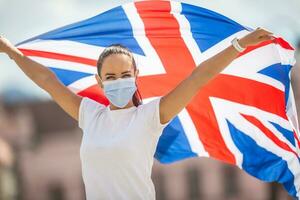 Frau im Gesicht Maske hält ein Vereinigtes Königreich Flagge während das bleibe stark Kampagne foto