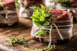 roh Steak eingewickelt mit Speck und frisch Kräuter auf ein hölzern Schneiden Tafel. foto